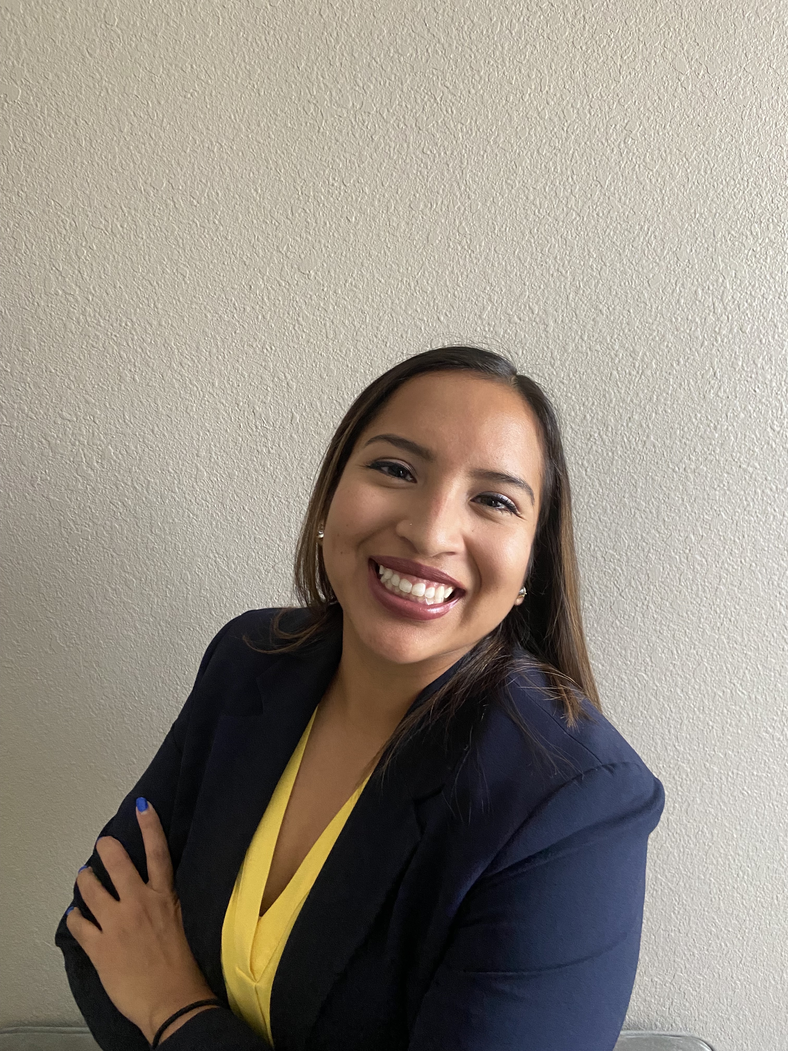 Jen is seen crossing her arms at the forefront, wearing a suit jacket over a yellow blouse.