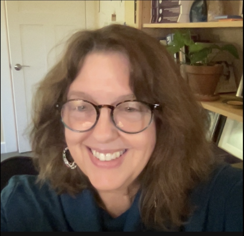 Kathy is seen at the forefront, with a bookcase in her backdrop.